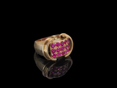 un gros plan d'une bague en or sertie de pierres roses sur un fond noir