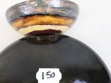a black vase sitting on a white surface with a label on it