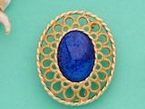 broche plaquée or ornée d'une pierre bleue entourée de coquillages sur fond turquoise