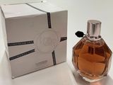 un flacon de parfum posé devant une boîte sur une surface blanche