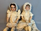 une paire de poupées anciennes en porcelaine assises l’une à côté de l’autre sur une surface grise