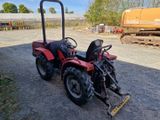 un petit tracteur rouge garé sur la terre battue