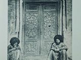 a black and white photo of two people sitting in front of a door