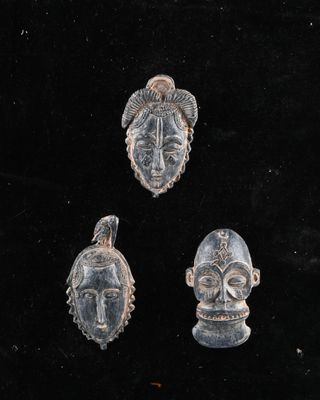 un ensemble de trois masques sculptés posés sur une surface noire