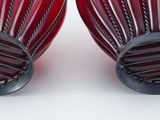 pair of red glass vases with black handles on a white surface