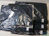 trois t-shirts noirs sont emballés dans du plastique sur une table