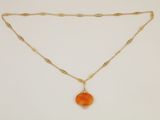 a gold necklace with an orange stone pendant on a gold chain