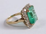 a close up of an emerald and diamond ring on a white surface