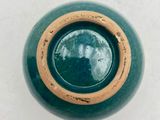 a green vase with a brown rim sitting on a white surface