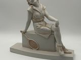 statue of a woman sitting on a box with a tennis racket in her hand