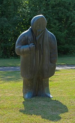 une statue représentant un homme coiffé d'une capuche, posée dans l'herbe