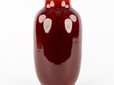 un vase rouge parsemé de taches blanches sur fond blanc