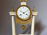 a white and gold clock sitting on top of a marble stand