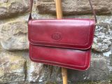 red leather handbag hanging on a wooden stick against a stone wall