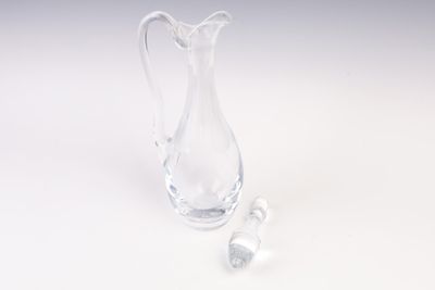 un pichet en verre transparent muni d'une anse, devant lequel se trouvent deux petits morceaux de verre
