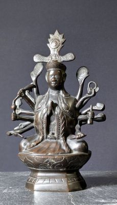 statue en bronze représentant une femme assise dans un bol, entourée de divers objets