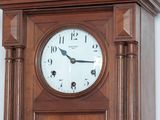 a wooden grandfather clock with a white face on the wall