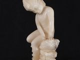 statue of a boy sitting on a rock with his hands on his knees