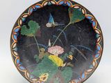une assiette noire sur laquelle est représentée une fleur et des feuilles