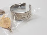 a silver bracelet with a leaf on it on a white surface