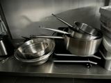 des casseroles et des poêles sont posées sur un plan de travail en acier inoxydable dans une cuisine