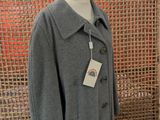 grey wool coat on a mannequin stand in front of a woven screen