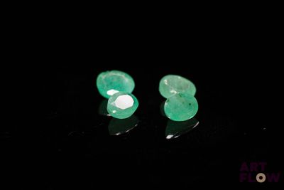 une paire de boucles d'oreilles en émeraude posées sur un fond noir