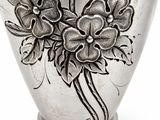 un vase en argent orné de fleurs, posé sur un fond blanc