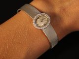 photo prise au niveau du poignet d'une femme portant une montre en argent avec une lunette sertie de diamants