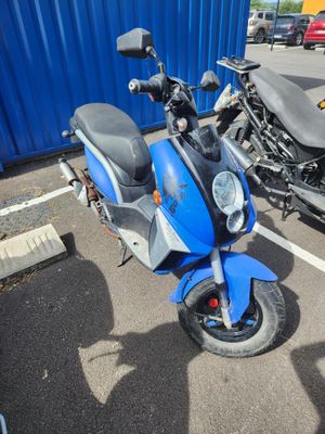 un scooter bleu garé sur un parking à côté d'une moto