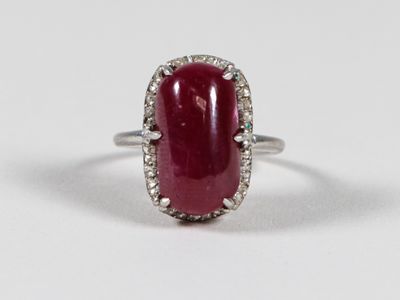a close up of a ring with a red stone surrounded by diamonds