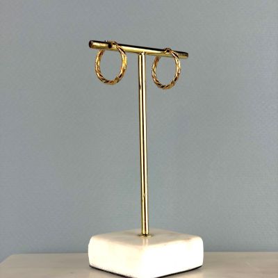 une paire de boucles d'oreilles créoles en or posée sur un socle en marbre, sur une table