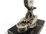 a silver clock on a marble stand with a bird on it