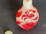 a red and white glass bottle with a red swirl on it