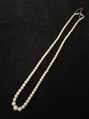 un collier de perles blanches avec un fermoir en or sur fond noir