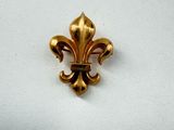un gros plan d'une broche en forme de fleur de lys dorée posée sur une surface blanche
