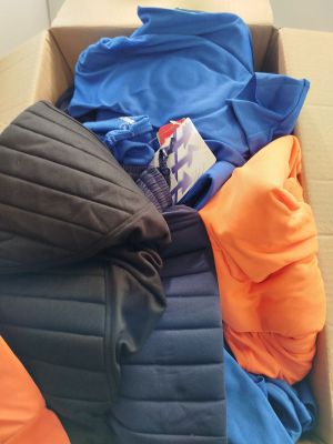 une boîte en carton remplie de vêtements et de couvertures, posée par terre