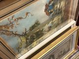 two framed paintings on a table in a room next to a mirror