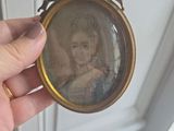 someone is holding a miniature picture of a woman in a gold frame