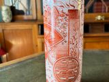 a red vase sitting on a table in front of a bookcase