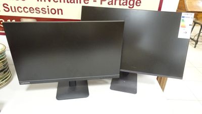 two computer monitors sitting on top of a table in front of a sign