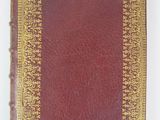 an old red book with gold trim sitting on top of a white surface