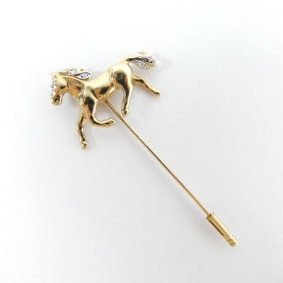 un gros plan d'une broche en forme de cheval en or sertie de diamants, sur fond blanc