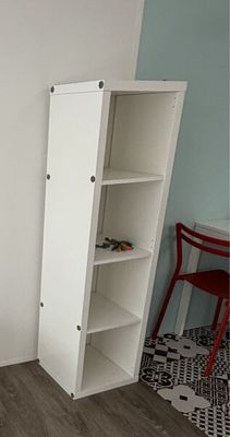 une armoire blanche dans un coin de la pièce, avec une chaise rouge à côté