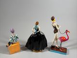 three figurines of a woman in a dress and a flamingo