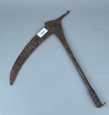 une vieille faux en bois rouillée, sur laquelle est accrochée une étiquette
