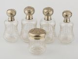 four glass bottles with gold tops and lids on a white surface