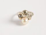 une photo d'une bague sertie d'un diamant et d'une perle sur un fond blanc