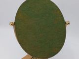 a green oval mirror on a gold stand on a white surface