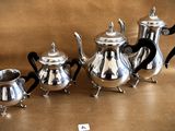 four silver teapots and two silver cups on a table